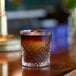 An Arcoroc Broadway rocks glass filled with a dark liquid on a bar.