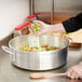 A person pouring chopped vegetables into a Vollrath Wear-Ever Classic Select aluminum brazier pan.