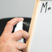 A hand spraying a white Expo spray bottle on a white board.