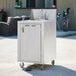 A silver portable sink cart with a white single bowl sink and a door.