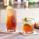 Two Acopa Cube beverage glasses filled with iced tea and garnished with mint and lemon on a table in a cocktail bar.