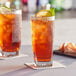 Two Acopa Cube beverage glasses filled with iced tea, lemon slices, and mint leaves.