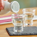 A person pouring sake into an Acopa Select sake shot glass on a table.