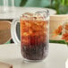 A clear plastic beverage pitcher filled with ice and brown liquid on a table.