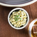 A Chef & Sommelier black stoneware ramekin filled with food next to a glass of liquid.