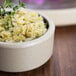 A Chef & Sommelier black stackable stoneware ramekin filled with food and a sprig of thyme on a table.