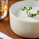 A white Chef & Sommelier stoneware bowl with a sprig of green plant sprouting out of it.