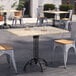 An Art Marble Furniture Kashmir White Granite Tabletop on a black metal table with a chair outside on a brick surface.