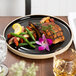 A Chef & Sommelier black dinner plate with a piece of meat and vegetables and a flower on the table.