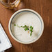 A stackable black stoneware bowl of soup with a sprig of thyme.