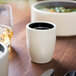 A white Chef & Sommelier stoneware cup with a black rim of liquid on a table.