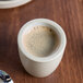 A Chef & Sommelier white stoneware espresso cup filled with coffee on a table next to a spoon.