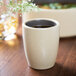 A Chef & Sommelier gray stoneware espresso cup filled with liquid on a table with a small white flower.