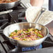 A person cooking food in a Vigor stainless steel fry pan on a stove.