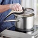 A person wearing a glove stirring soup in a Vigor stainless steel sauce pan on a stove.