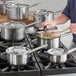 A person cooking soup in a Vigor stainless steel sauce pan on a stove.