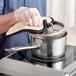 A gloved hand using a glove to hold a Vigor stainless steel sauce pan.