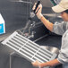 A woman in a white shirt and gloves washing a Cambro vented shelf plate in a kitchen sink.