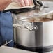 A person cleaning a Vigor stainless steel sauce pot on a counter.