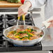 A woman cooking food in a Vigor stainless steel fry pan on a stove.