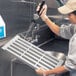 A woman in a white shirt and gloves using a Cambro vented shelf end plate to wash dishes in a school kitchen.