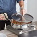 A person cooking food in a pan on a stove using a Vigor SS1 Series stainless steel lid.
