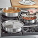 A woman using a Vigor stainless steel saute pan with a helper handle to cook food on a stove.