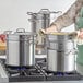 A woman uses a Vigor stainless steel pasta cooker on a stove top.