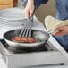 A person cooking meat in a Vigor stainless steel non-stick fry pan.