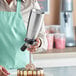 A person pouring whipped cream from an iSi stainless steel whipped cream dispenser onto a cake.