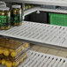 A white Cambro vented shelf with a variety of food items on it, including a jar of pickles, beans, and a lemon.