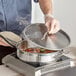 A man using a Vigor stainless steel saute pan to cook food on a stove.