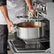 A man using a Vigor stainless steel brazier to cook on a stovetop.