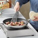 A person cooking potatoes in a Vigor stainless steel non-stick fry pan with a spatula.