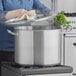 A woman using a Vigor stainless steel lid on a large pot on a stove.