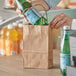 A hand putting a green bottle of soda into a Duro natural kraft paper bag with handles.