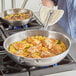 A person using a Vigor stainless steel fry pan to cook food on a stove.