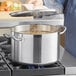 A person cooking in a Vigor stainless steel stock pot on a stove.