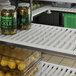 A white Cambro vented shelf with jars of food on a white counter.