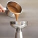 A person using a iSi stainless steel funnel to pour liquid into a silver pot.