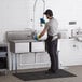 A man in a black shirt and blue pants using a Regency stainless steel three compartment sink in a professional kitchen.