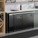 A black solid door back bar refrigerator with LED lighting installed under a countertop.