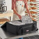 A woman in an apron using a black Sterno catering food carrier to transport a plastic container of bread.