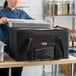 A woman holding a tray on top of a large black insulated catering food carrier.