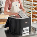 A woman wearing an apron putting a tray in a small black insulated food carrier bag.