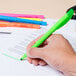 A hand holding a Bic Brite Liner green pen writing on a piece of paper.