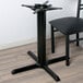 A black Lancaster Table & Seating table base next to a chair with a wooden seat.