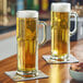 Two Libbey Frankfurt beer mugs filled with beer on a table with a bowl of nuts.