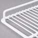 A white coated wire top shelf for deli and display cases with a white metal rack on top.