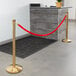 A Lancaster Table & Seating gold rope crowd control barrier set with a red rope in use in front of a reception desk.